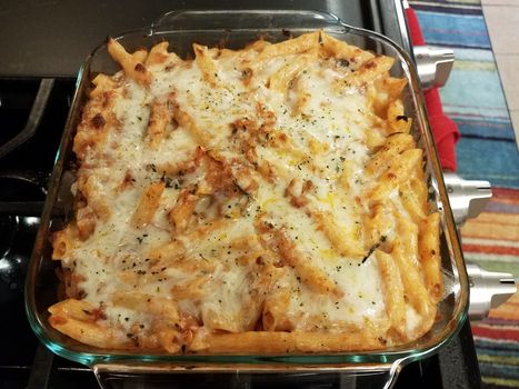 baked hot cheesy penne pasta in glass container on stove