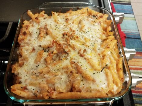 baked hot cheesy penne pasta in glass container on stove