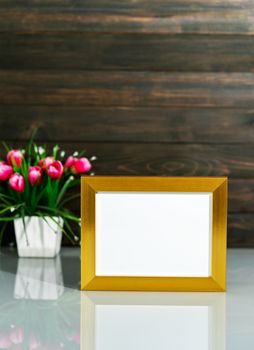 Picture mock up with golden frame and Artificial flower vase bouquet over table with wood wall background