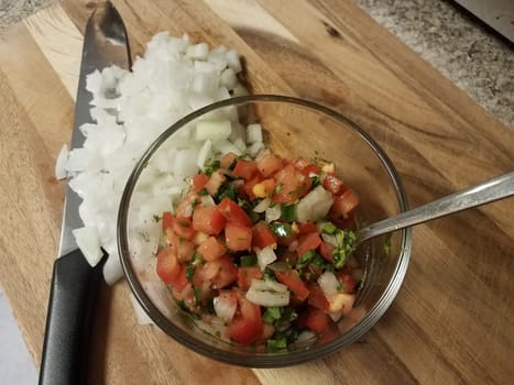 tomatoes and onions and glass bowl on wood cutting board