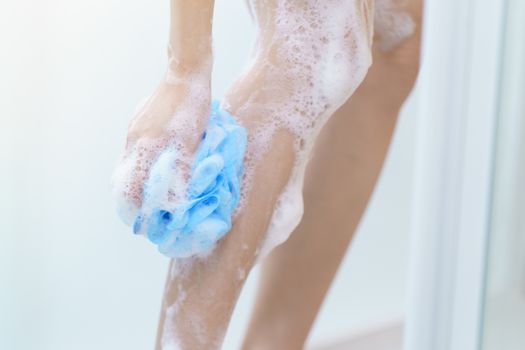 Woman washing her leg with bath sponge.