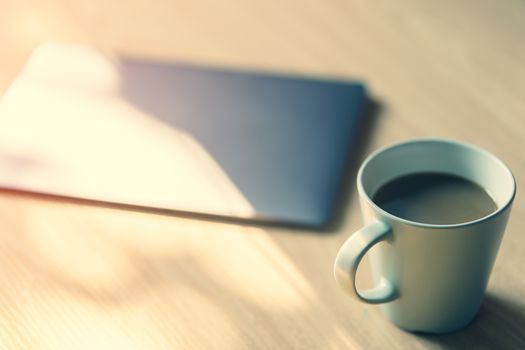 Work desk with a laptop computer, a cup of coffee, with morning sunlight. vintage style.