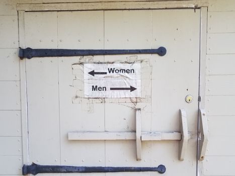 white wood door with men and woman bathroom sign and arrows