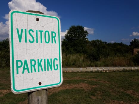 weathered white and green visitor parking sign and grass