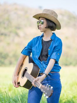 Young asian woman short hair wear hat  and carry her guitar  in grass field countryside Thailand