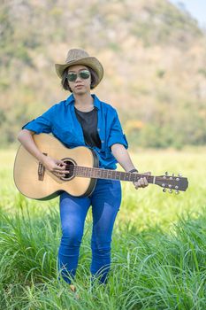 Young asian woman short hair wear hat  and carry her guitar  in grass field countryside Thailand