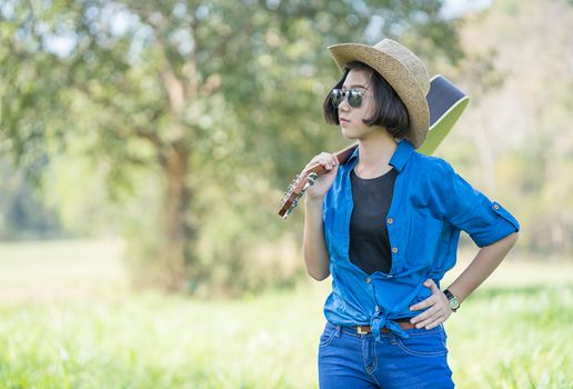 Young asian woman short hair wear hat  and carry her guitar  in grass field countryside Thailand