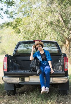 Young asian women short hair wear hat and sunglasses carry her guitar bag ,sit on pickup truck in countryside Thailand