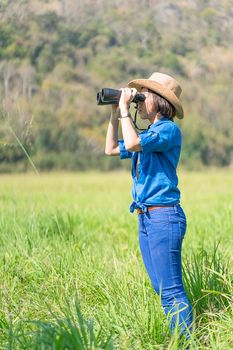 Young asian woman short hair wear hat and hold binocular in grass field countryside Thailand