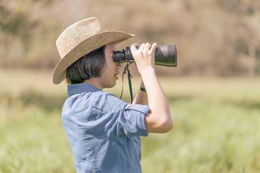 Young asian woman short hair wear hat and hold binocular in grass field countryside Thailand