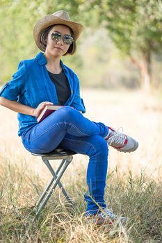 Young asian women short hair wear hat and sunglasses read a book ,sit on chair in countryside Thailand