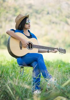 Young asian women short hair wear hat and sunglasses sit playing guitar in grass field countryside Thailand