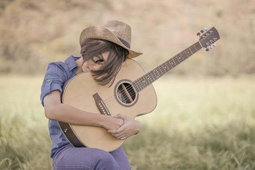 Young asian women short hair wear hat and sunglasses sit playing guitar in grass field countryside Thailand