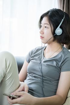 Close up young asian woman short hair listening music from mobile phone on the couch