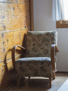 old upholstered wooden armchair with flower pattern under window