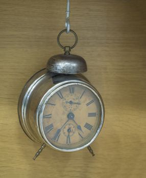 vintage retro metal alarm clock for for waking up hanging from hook on beige wooden background, time concept.