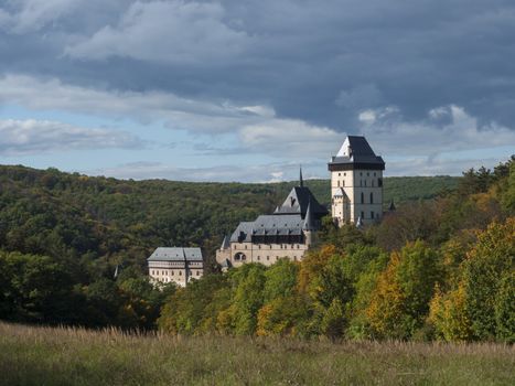 Karlstejn gothic state castle near Prague, the most famous castle in Czech Republic with grass meadow and autumn colored trees and forest. Blue sky clouds background. Located near Prague..