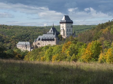 Karlstejn gothic state castle near Prague, the most famous castle in Czech Republic with grass meadow and autumn colored trees and forest. Blue sky clouds background. Located near Prague..