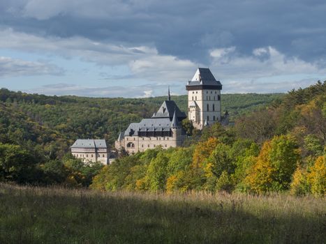 Karlstejn gothic state castle near Prague, the most famous castle in Czech Republic with grass meadow and autumn colored trees and forest. Blue sky clouds background. Located near Prague..