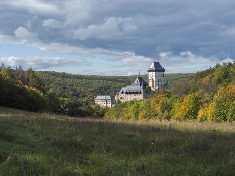 Karlstejn gothic state castle near Prague, the most famous castle in Czech Republic with grass meadow and autumn colored trees and forest. Blue sky clouds background. Located near Prague..