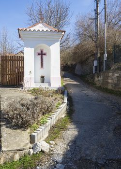 small white wayside shrine, road blessing or Gods torture with cross next village road curve in Srbsko, Czech republic.