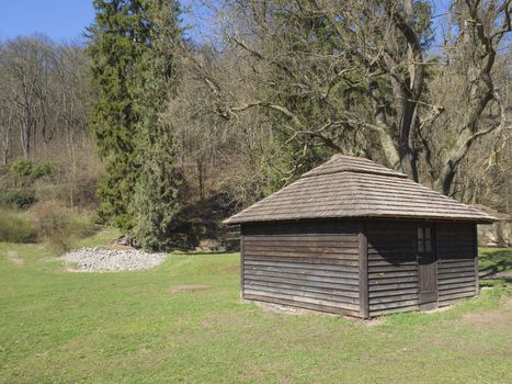 old historical log cabin house in spring forest, grass and trees in the countryside of central Bohemian region on on sunny day, blue sky.