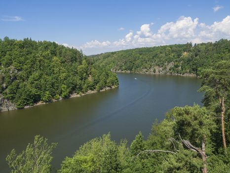 view from bridge zvikov on otava and vltava river with green tree forest rocky shore blue water, boat and blue sky white clouds background