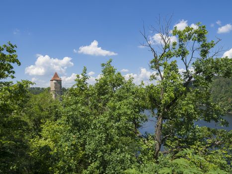 view on medieval czech castle Zvikov round tower and river Vltava, green trees in foreground  blue sky, white clouds background 