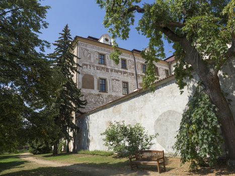 Czech Republic, Benatky nad Jizerou, July 28, 2018: Renaissance style castle with Sgraffito decorated facade, park, footpath, green trees garden and wooden bench, sunny summer day