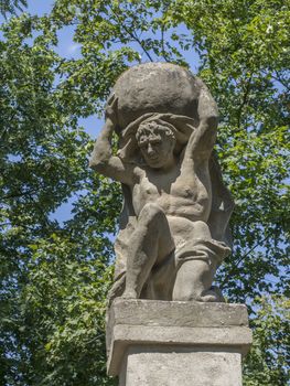 Stone men figure carrying stone, baroque statue from Greek mythology of Sisyphus or Sisyphos, garden, green trees background, czech republic