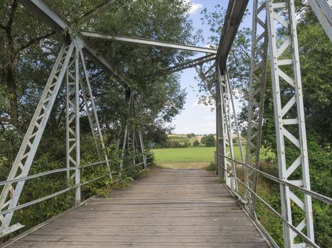 Footbridge across Jizera river made of wood and metal steel girder with view on trees and rural summer landscape with fields