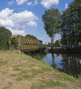 old arc bridge across Jizera river made metal steel girder with view on trees and village summer landscape, blue sky