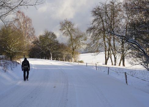 men figure in black clothes with backpack walking on snow covered asphalt road in winter forest