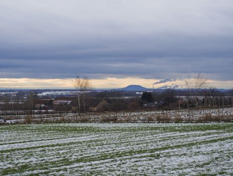 Winter rural landscape with green snow covered fields at sunset. View of the mountain Rip hill with smoking chimney, popular pilgrimage place, central Bohemian region. Czech Republic