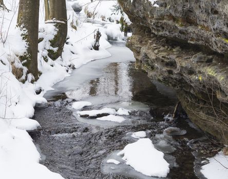 snow covered partly frozen forest water stream creek with sand stone rock, winter landscape