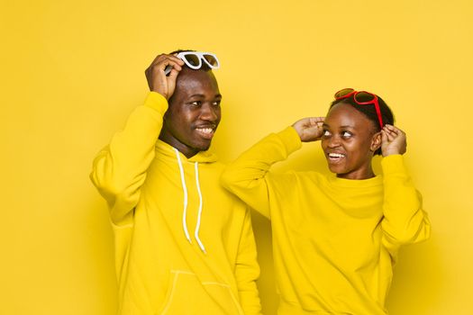 Man and woman of African appearance smile yellow sweatshirts studio dark glasses