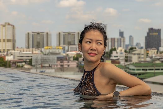 Short haired young woman relaxes in the roof top outdoor swimming pool and enjoying in sunny day. Summer vacation concept.