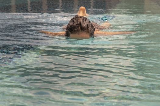 Short haired young woman swimming in the swimming pool with her reflection in it. Healthy happiness lifestyle.