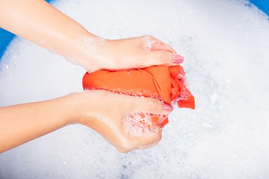 Closeup young Asian woman use hands washing color clothes in basin with detergent have soapy bubble water, studio shot background, laundry concept