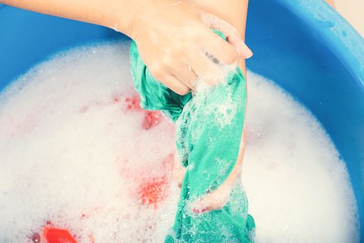 Closeup young Asian woman use hands washing color clothes in basin with detergent have soapy bubble water, studio shot background, laundry concept