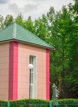 Resort building in pink with a green roof against the background of trees and a Park, summer day.