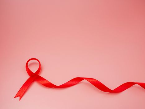 Red ribbon on pink background. world aids day concept, symbol of human immunodeficiency virus disease.