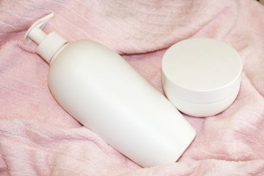 white cosmetic bottle and cream jar on pink terry cloth close up