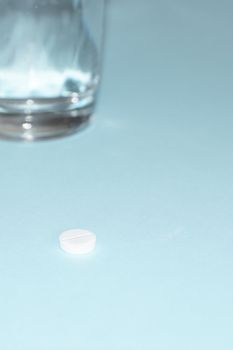 pill and glass of water on blue background.