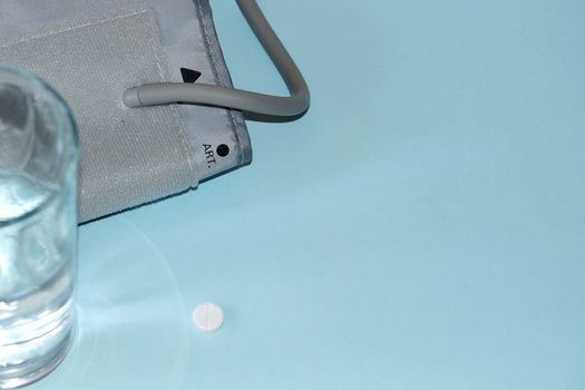 tonometer, pill and glass of water on blue background.