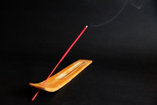 smoking incense stick on wooden stand on black background