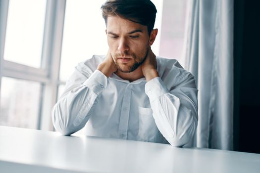 A puzzled man at work sits at a table and has a cropped look