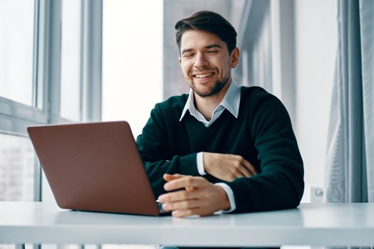 Happy man at work looking at a laptop and sitting near the window