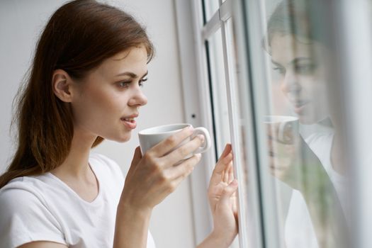 Happy woman with a cup of coffee near the window looks at the natur