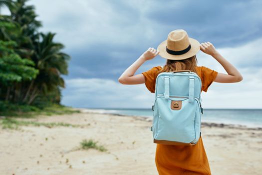 Beautiful traveler in a sundress with a backpack on his back on an island by the ocean